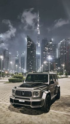 a silver jeep parked in front of a city at night with lights shining on the buildings