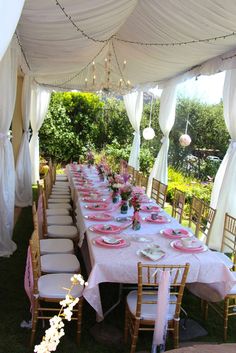 a long table set up with pink and white linens for an outdoor wedding reception