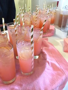 many glasses filled with pink liquid and straws sitting on a table next to each other