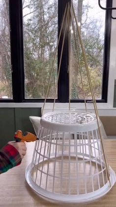 a white birdcage sitting on top of a wooden table next to a window