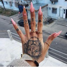 a woman's hand with pink nail polish and tattoos on her left palm, in front of a city street