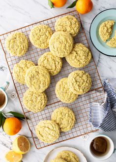 lemon cookies cooling on a wire rack with oranges in the background and two cups of tea next to them