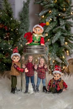 three children are standing in front of a glass jar with an elf on it and another child is holding their hand out