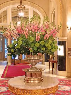 a vase filled with pink and green flowers sitting on top of a table in front of a doorway