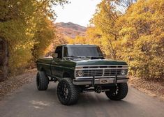 a green truck driving down a road surrounded by trees