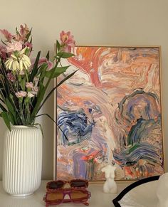 a vase filled with flowers sitting on top of a white table next to a painting