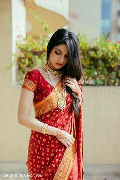 a woman in a red and gold sari is looking down at her necklaces