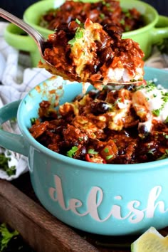 a spoon full of chili and cheese in a blue bowl with the word delish on it