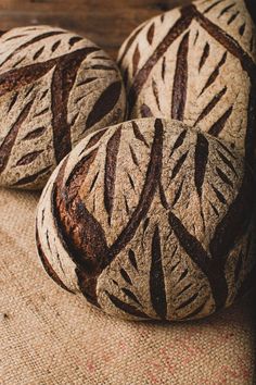 three loaves of bread sitting on top of a burlly cloth covered table