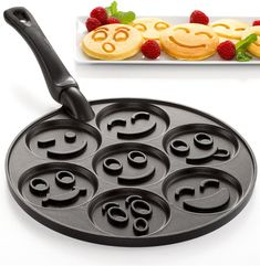 a pan with smiley faces on it next to some raspberries and pancakes in the background