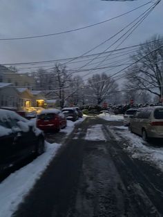 cars parked on the side of a snow covered road in front of houses and power lines