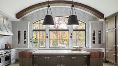 a large kitchen with an arched window and two pendant lights hanging from the ceiling over the island