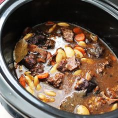 a slow cooker filled with beef stew and pine nuts