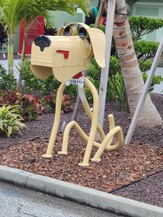 a yellow dog mailbox sitting on top of a sidewalk next to a palm tree