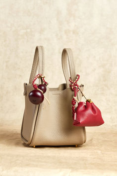 two small purses sitting next to each other on top of a wooden table with a cherry hanging from the handle