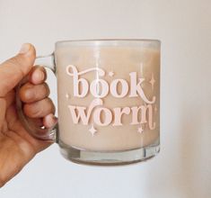 a person holding a coffee mug with the words book worm on it in pink lettering