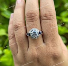 a woman's hand with a diamond and blue sapphire engagement ring on it, surrounded by greenery