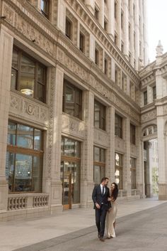 a man and woman are walking down the street in front of an old city building