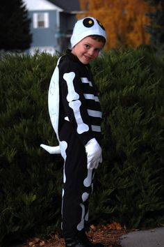 a young boy dressed up as a skeleton in front of some bushes and trees with his hands on his hips