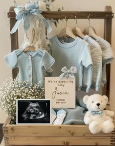 a teddy bear sitting next to baby's clothes and other items in a wooden crate