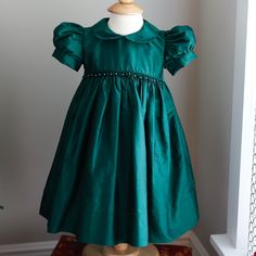 This Strasburg Emerald Green Dress Size 12 Months Is Most Gorgeous!!! Made Of 100% Luxurious Dupioni Silk. Smocking At Waist With Hand Embroidery Emerald Rosettes With White Pearls In Between. Sweet Peter Pan Collar That Is Edged In Matching Piping. Waist Is Trimmed In Matching Piping Also. Short Puff Sleeves Are Finished With A 1 Inch Matching Silk Band.Upper Button Back With Matching Silk Fabric Buttons (High-End Detail). A Wide Tie Back Sash Is The Finishing Touch With This Exquisite Strasbur Green Fitted Princess Dress With Short Sleeves, Classic Short Sleeve Dress For Dress-up, Fitted Green Dress For Baptism, Emerald Green Dress, Emerald Green Dresses, Cotton Slip, Fabric Buttons, Dupioni Silk, Dress Silk