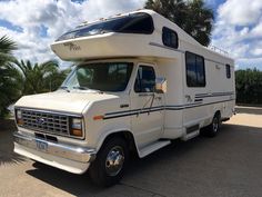 an rv is parked on the street in front of palm trees and blue sky with clouds