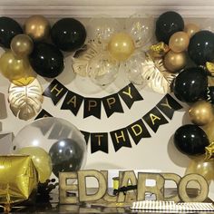 a birthday party with balloons and streamers on the wall, black and gold decorations