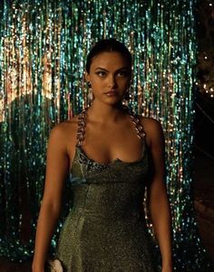 a woman in a dress standing next to a wall with lights on it and a handbag hanging from her shoulder