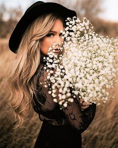 a woman in a black dress holding a bunch of white flowers with her face close to the camera