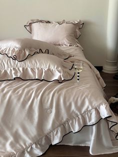 a bed with white sheets and black ruffles on the comforter has a glass of wine in front of it