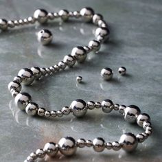 a silver bead necklace on a table with other beads in the foreground and an object to the side