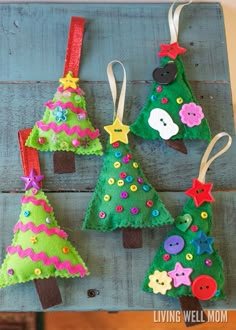 christmas tree ornaments made from felt and buttons on a wooden board with ribbon hangings