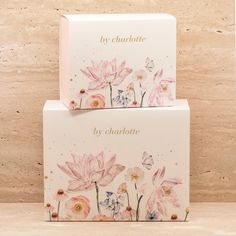 two boxes with pink flowers on them sitting on top of a wooden table in front of a wall