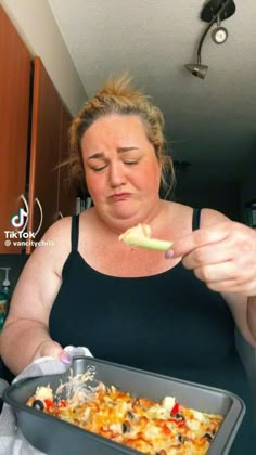 a woman eating food from a pan in the kitchen