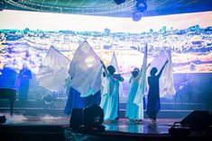 some people are standing on a stage with their arms in the air and one person is holding two white flags