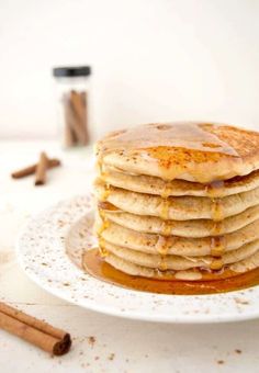 a stack of pancakes covered in syrup on a white plate with cinnamon sticks next to it