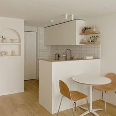 a small kitchen with white walls and wooden flooring next to a dining room table