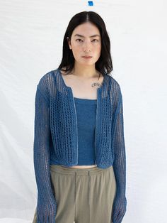 a woman standing in front of a white backdrop wearing a blue sweater and khaki pants