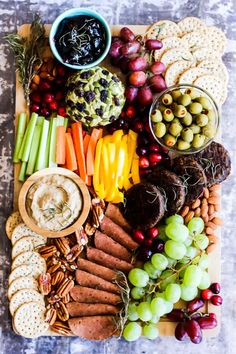 a platter filled with crackers, grapes, apples, celery, carrots and other snacks