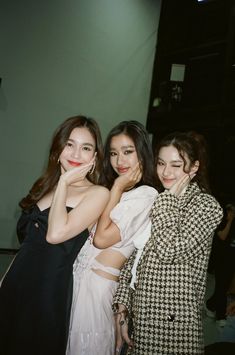 three young women standing next to each other in front of a wall and posing for the camera