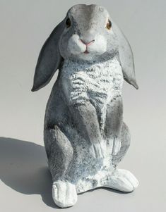 a gray rabbit statue sitting on top of a white floor next to a grey wall