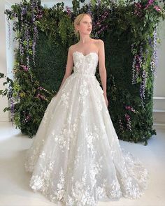 a woman in a white wedding dress standing next to a green wall with flowers on it