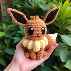 a small crocheted pokemon doll sitting on top of a persons hand in front of some plants