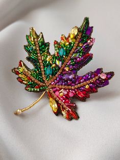 a colorful leaf brooch sitting on top of a white cloth