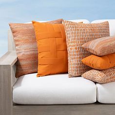 a white couch with orange and brown pillows on it's back end, in front of a blue sky