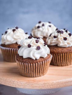 three cupcakes with white frosting and chocolate chips on top sitting on a wooden tray