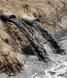 two large pipes that are connected to each other in the water near some dirt and grass