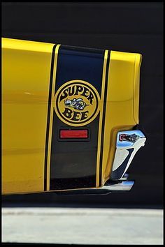 a close up of the side of a yellow and black super bee car parked in front of a building