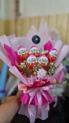 a hand holding a bunch of chocolate eggs wrapped in pink paper and tied with ribbon