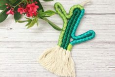 the green and white tassel is next to red flowers on a wooden table with greenery